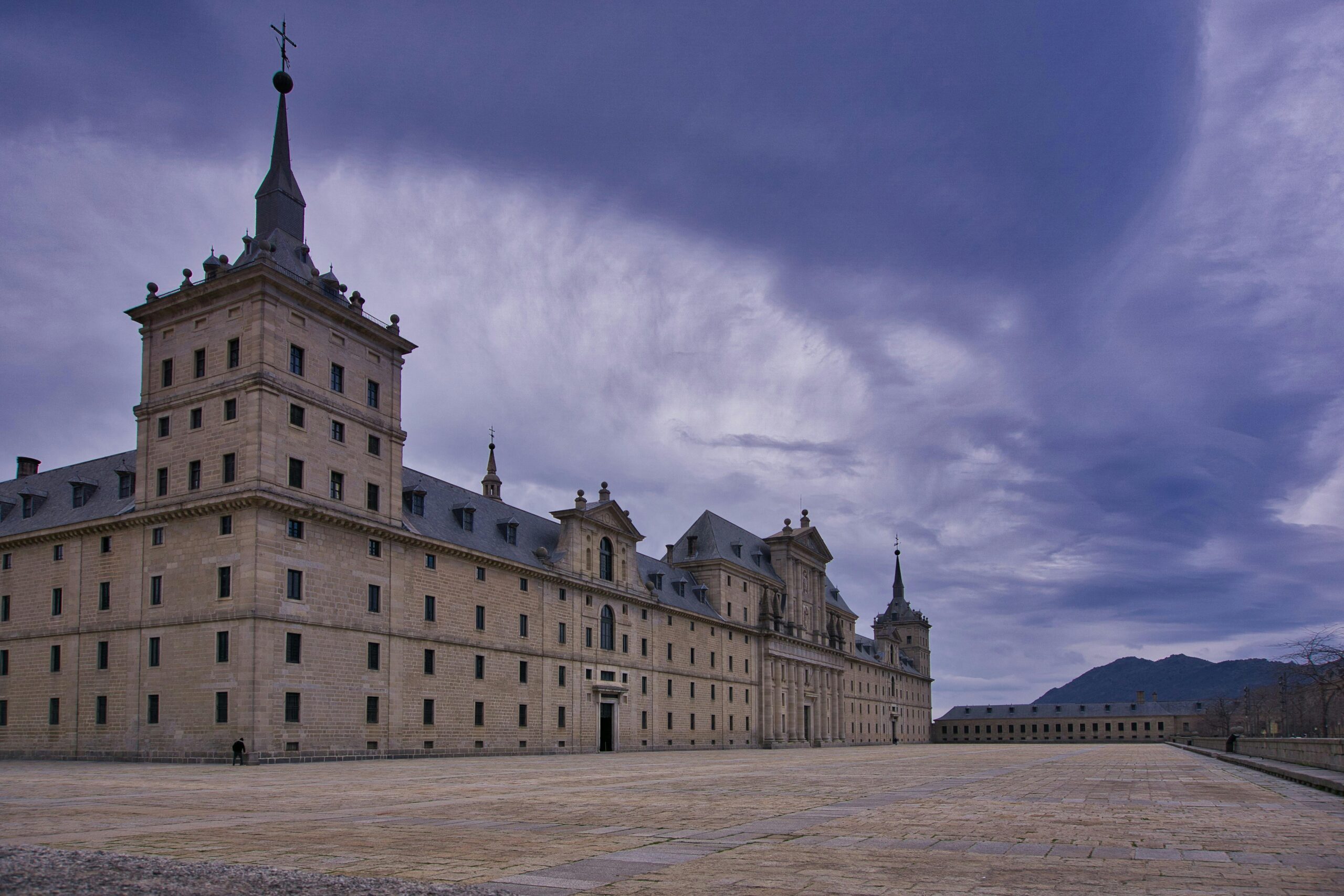Explore the majestic El Escorial Monastery in Spain, framed by a vivid sky. Perfect for history and architecture enthusiasts.
