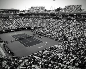 A black and white photo capturing a thrilling tennis match in a crowded outdoor stadium.