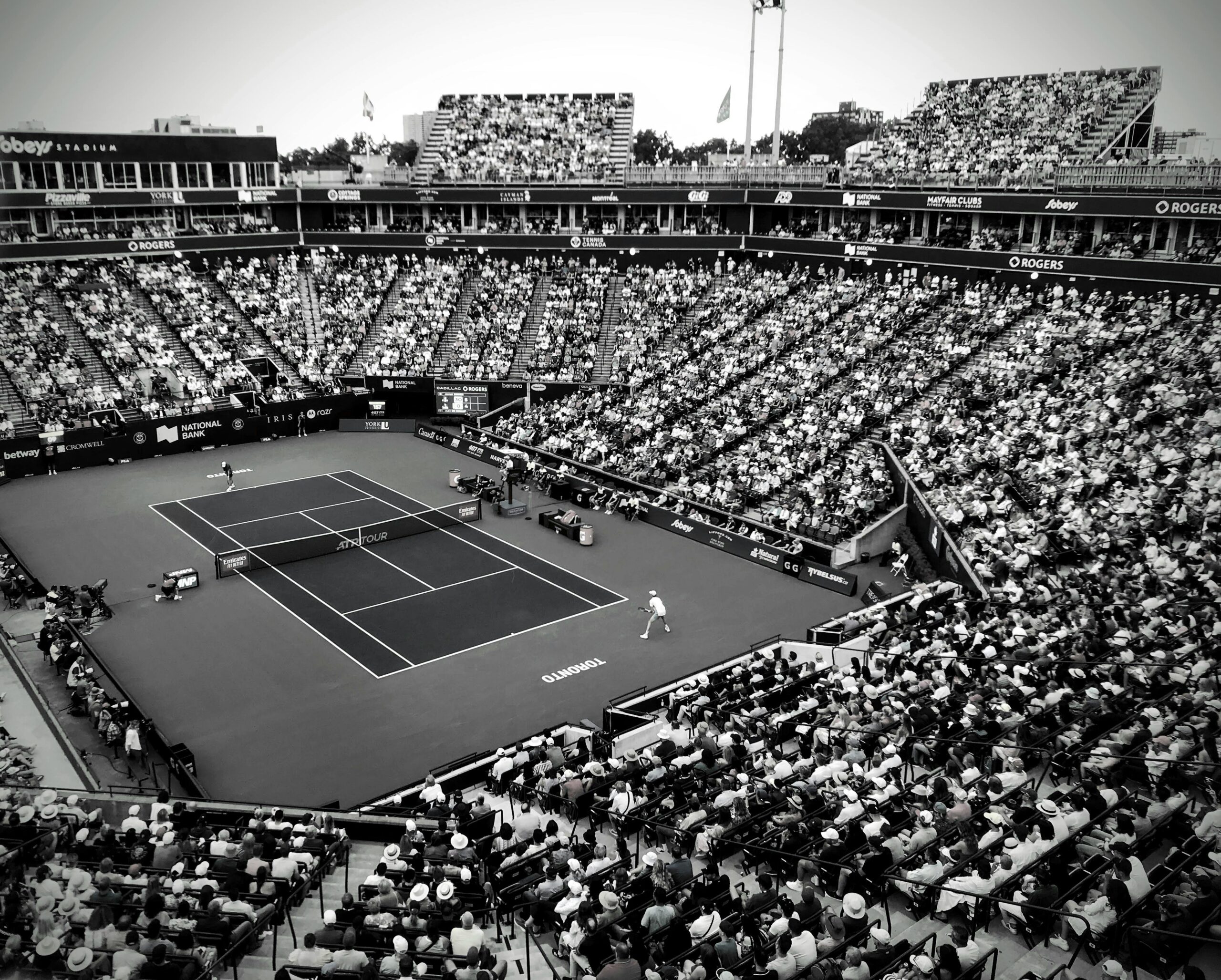 A black and white photo capturing a thrilling tennis match in a crowded outdoor stadium.