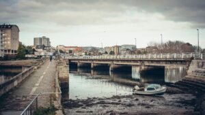 A peaceful urban landscape featuring a bridge over a river in Burgo, Spain, with buildings and a motorboat.