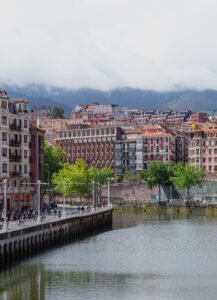 A vibrant view of Bilbao's architecture and riverbanks under cloudy skies.